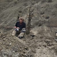 David Asmus sitting on rock writing in a field notebook.
