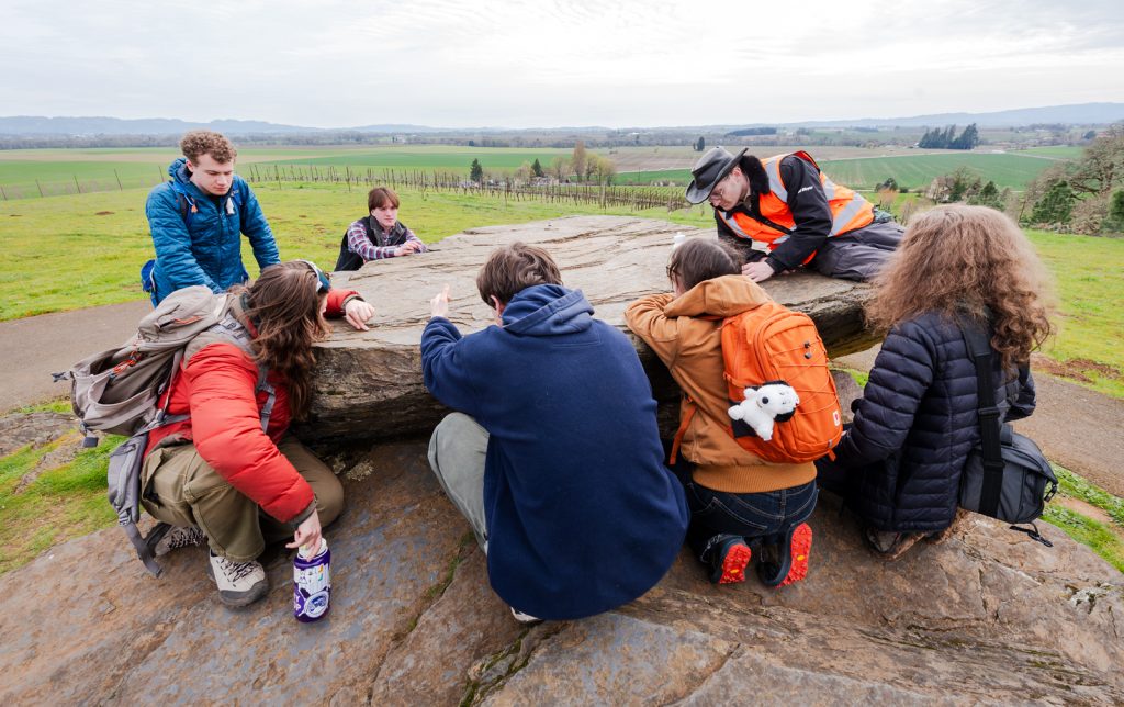 Students sitting around a large boulder.