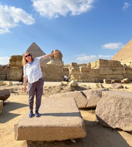 Donna Whitney standing on a rock slab with a pyramid behind her.